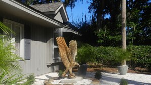 A house with a stone bird sculpture in the front yard, surrounded by potted plants and a gravel path. - Rates Jan through mid March 2027 are reduced for longer stays. (Hilton Head Island)