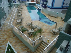 Un espace piscine aménagé sur le toit, avec des chaises longues et des tables, entouré d’une terrasse carrelée et d’un escalier menant à un niveau supérieur.