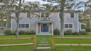 A two-story house with a front porch, a driveway, and a well-maintained lawn. - Modern, luxury 5-bed, 4.5-bath w/full basement! Now booking for 2026! (Oak Bluffs)
