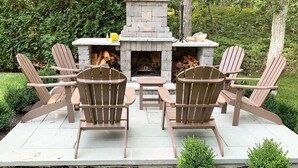 A stone fire pit with seating around it, surrounded by greenery. - Modern, luxury 5-bed, 4.5-bath w/full basement! Now booking for 2026! (Oak Bluffs)