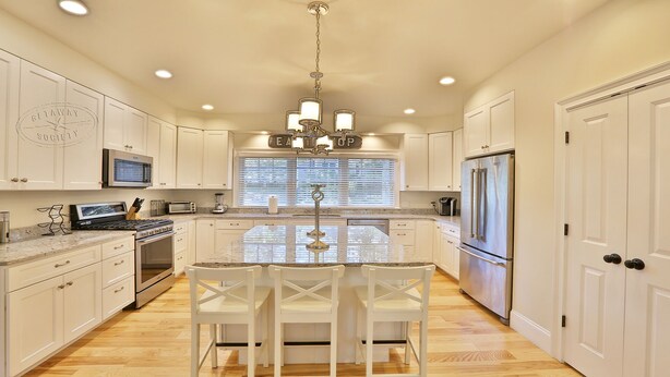 A spacious kitchen with white cabinetry, a central island with seating, a stainless steel refrigerator, and a built-in oven. - Modern, luxury 5-bed, 4.5-bath w/full basement! Now booking for 2026! (Oak Bluffs)
