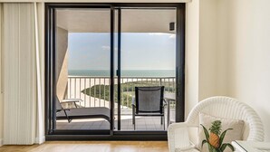 A balcony with a view of the sea, a chair, and a table.