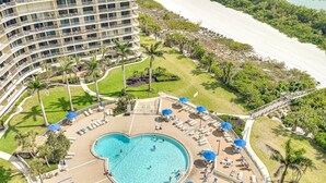 A hotel with a large pool, multiple balconies, and a beach area.