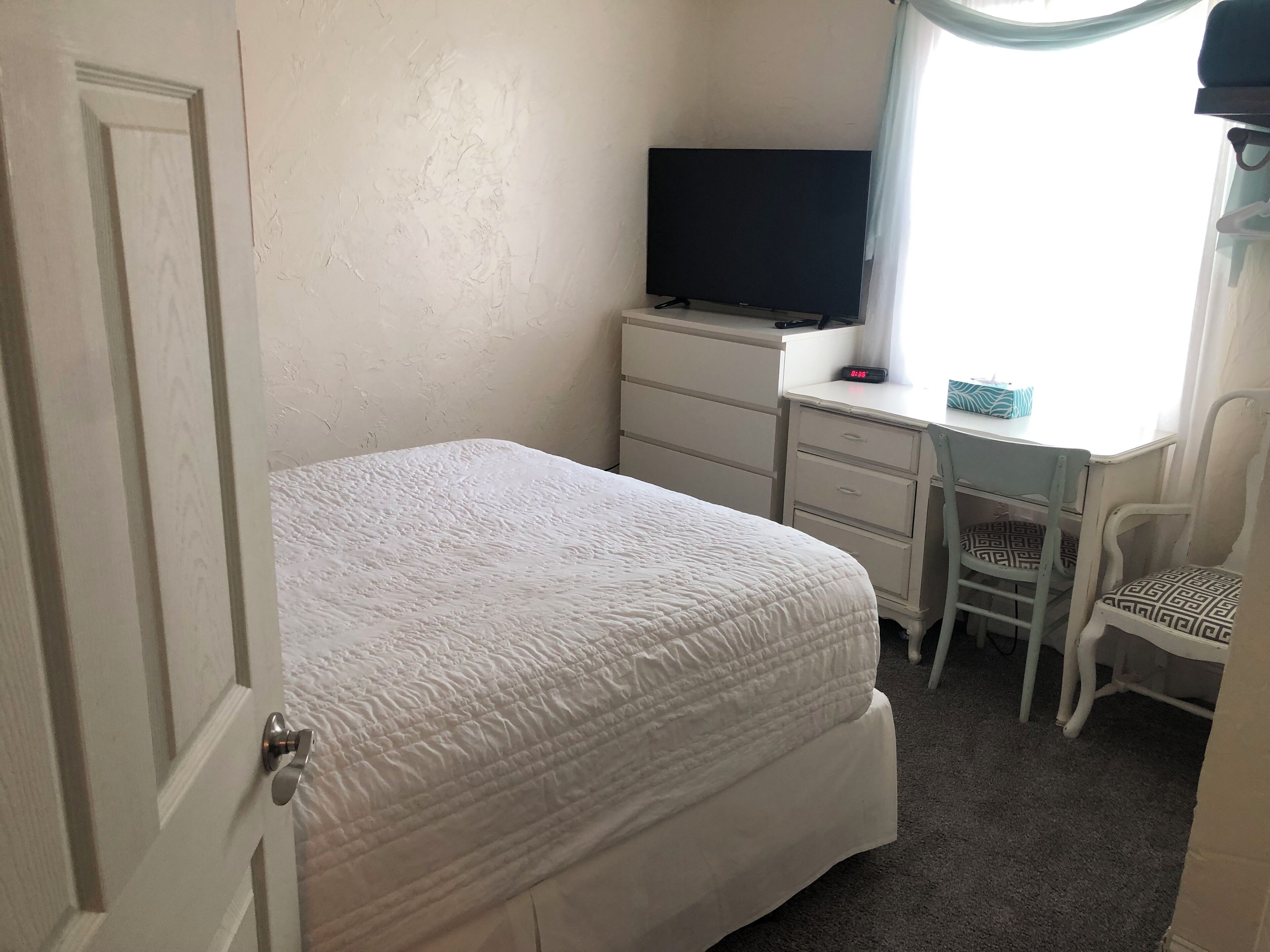 A bedroom with a bed, a desk with a chair, a television, and a clock.