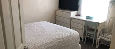 Een slaapkamer met een bed, een bureau met stoel, een televisie en een klok.