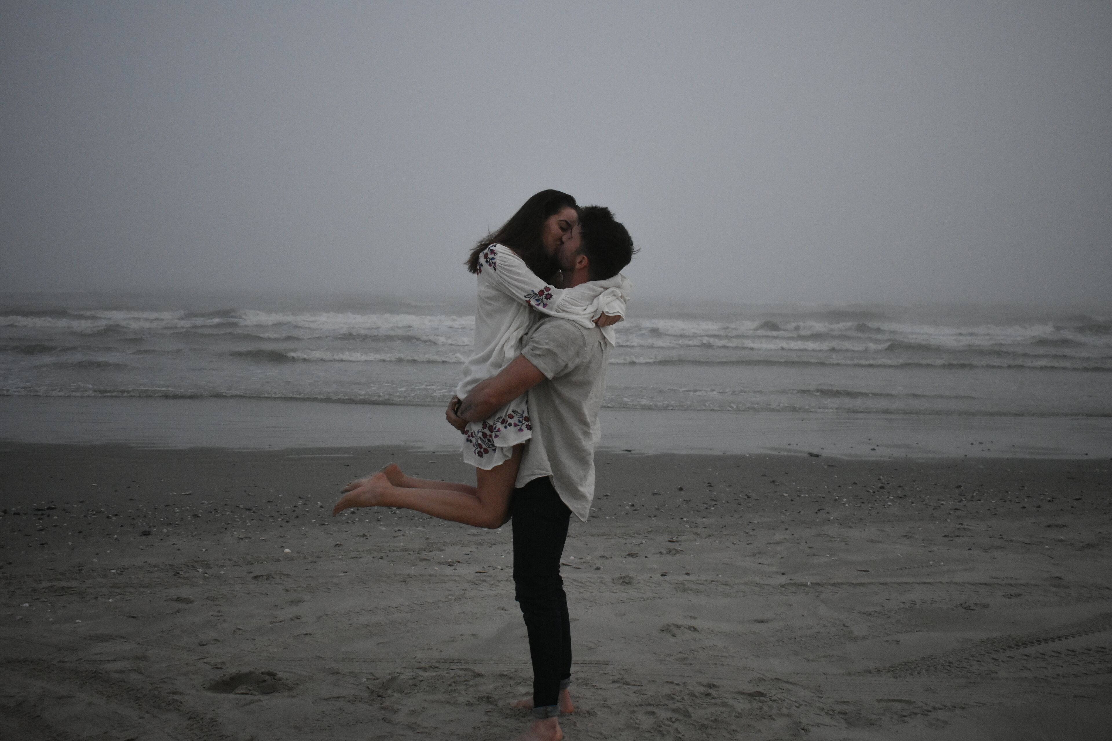 Ein Paar umarmt sich am Strand, im Hintergrund Wellen.