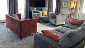 A living room with a sofa, armchair, TV, and artwork on the wall.