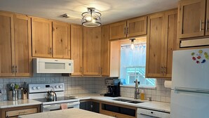 A kitchen with wooden cabinets, a central island with stools, a refrigerator, and a window with curtains.
