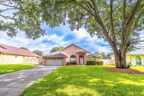 A residential house with a front yard, driveway, and a large tree.