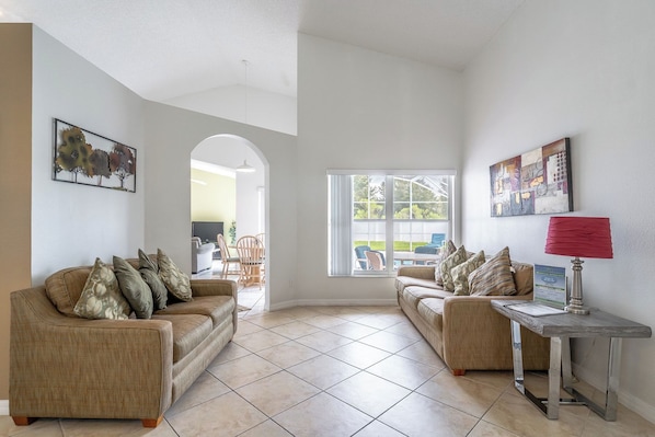 A living room with two sofas, a coffee table, and a lamp. There is a large window with a view of the outdoors.