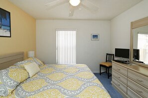 Ein Schlafzimmer mit Bett, Kommode, Stuhl, Fernseher und einem Fenster mit Jalousien.