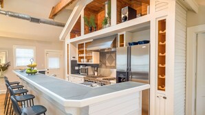 Eine moderne Küche mit einer zentralen Kochinsel, Edelstahlgeräten und einer Holzbalkendecke.