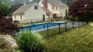 A house with a swimming pool surrounded by a black fence, a brick chimney, and a well-maintained lawn. - Walk to the Beach, Heated Salt Water Pool, Central AC (Dennis)