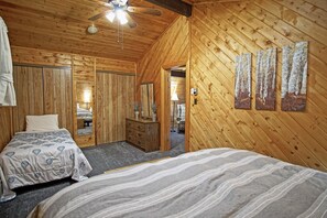 A cozy log cabin bedroom with two beds, a dresser, a mirror, and a ceiling fan.