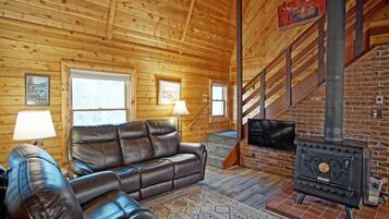A wooden cabin interior with a leather sofa, a fireplace, and a staircase.