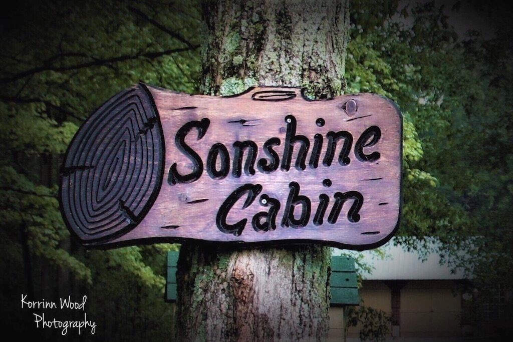 A wooden sign with the text "Sunshine Cabin" mounted on a tree.