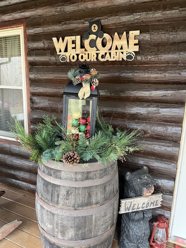 A wooden cabin with a 'WELCOME TO OUR CABIN' sign, a lantern with pine cones and greenery, and a 'WELCOME' sign on a bear statue. - Sonshine Cabin is your own private park. With wildlife or a hike to the creek. (Madison)