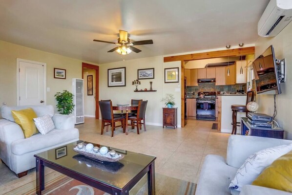 A living room with a dining area, kitchen, and a ceiling fan.