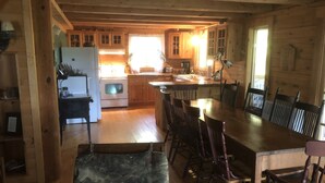 A wooden cabin interior with a kitchen, dining area, and a large window.