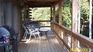 A wooden deck with outdoor furniture, a grill, and a scenic view of trees.