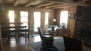 A rustic interior with wooden floors, a stone fireplace, and a dining area with chairs and a table.