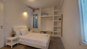 Quarto com cama, mesa de cabeceira, abajur e roupeiro embutido com prateleiras.