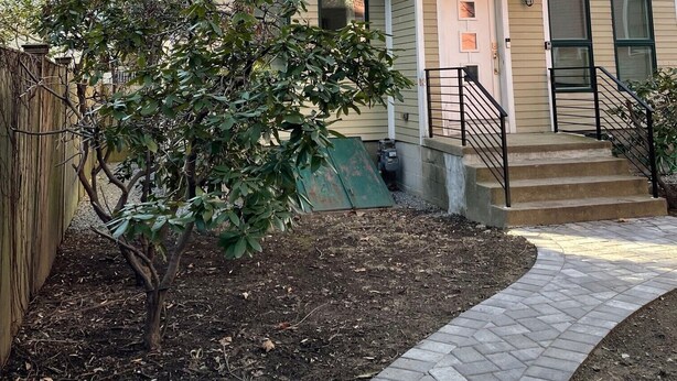 A two-story residential building with a balcony, a small garden area, and a paved walkway.