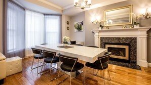 Un coin repas avec une table blanche et des chaises noires, une cheminée et un lustre.