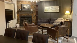 A living room with a fireplace, a sofa, a coffee table, and a dining area. - Newly Renovated Mountain Condo in Convenient Location (Whitefish)