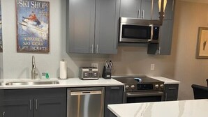 A modern kitchen with grey cabinets, stainless steel appliances, a microwave, a toaster, and a dishwasher. - Newly Renovated Mountain Condo in Convenient Location (Whitefish)