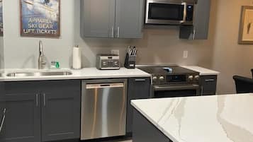 A modern kitchen with grey cabinets, a stainless steel dishwasher, a microwave, and a built-in oven.