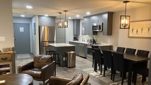 A modern kitchen with grey cabinets, stainless steel appliances, and a dining area with leather chairs and a round table. - Newly Renovated Mountain Condo in Convenient Location (Whitefish)