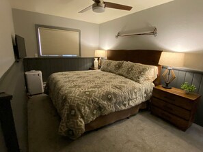 A bedroom with a bed, bedside lamps, a nightstand, a ceiling fan, a window with blinds, and a radiator. - Newly Renovated Mountain Condo in Convenient Location (Whitefish)