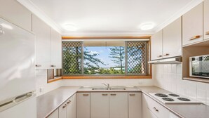 Eine moderne Küche mit weißen Schränken, einem eingebauten Herd und einem Fenster mit Blick auf Bäume.
