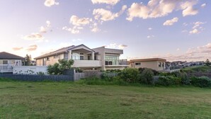 A modern residential area with houses, a grassy field, and a clear sky with clouds. - Kiama Dream – Absolute Waterfront | Panoramic Ocean Views | Large Groups (Kiama)