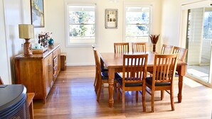 A dining area with a wooden table and chairs, a cabinet with a lamp, and a painting on the wall. - Kiama Dream – Absolute Waterfront | Panoramic Ocean Views | Large Groups (Kiama)