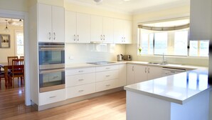 A modern kitchen with white cabinets, stainless steel appliances, and a large window providing natural light. - Kiama Dream – Absolute Waterfront | Panoramic Ocean Views | Large Groups (Kiama)
