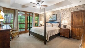 A bedroom with a four-poster bed, a ceiling fan, a stone wall, and large windows. - Secluded 40 Acres Near Table Rock, Stunning Views, Games, Community Pool & Car Charger (Blue Eye)