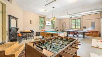 A spacious living room with a foosball table, a pool table, and a television mounted on the wall.