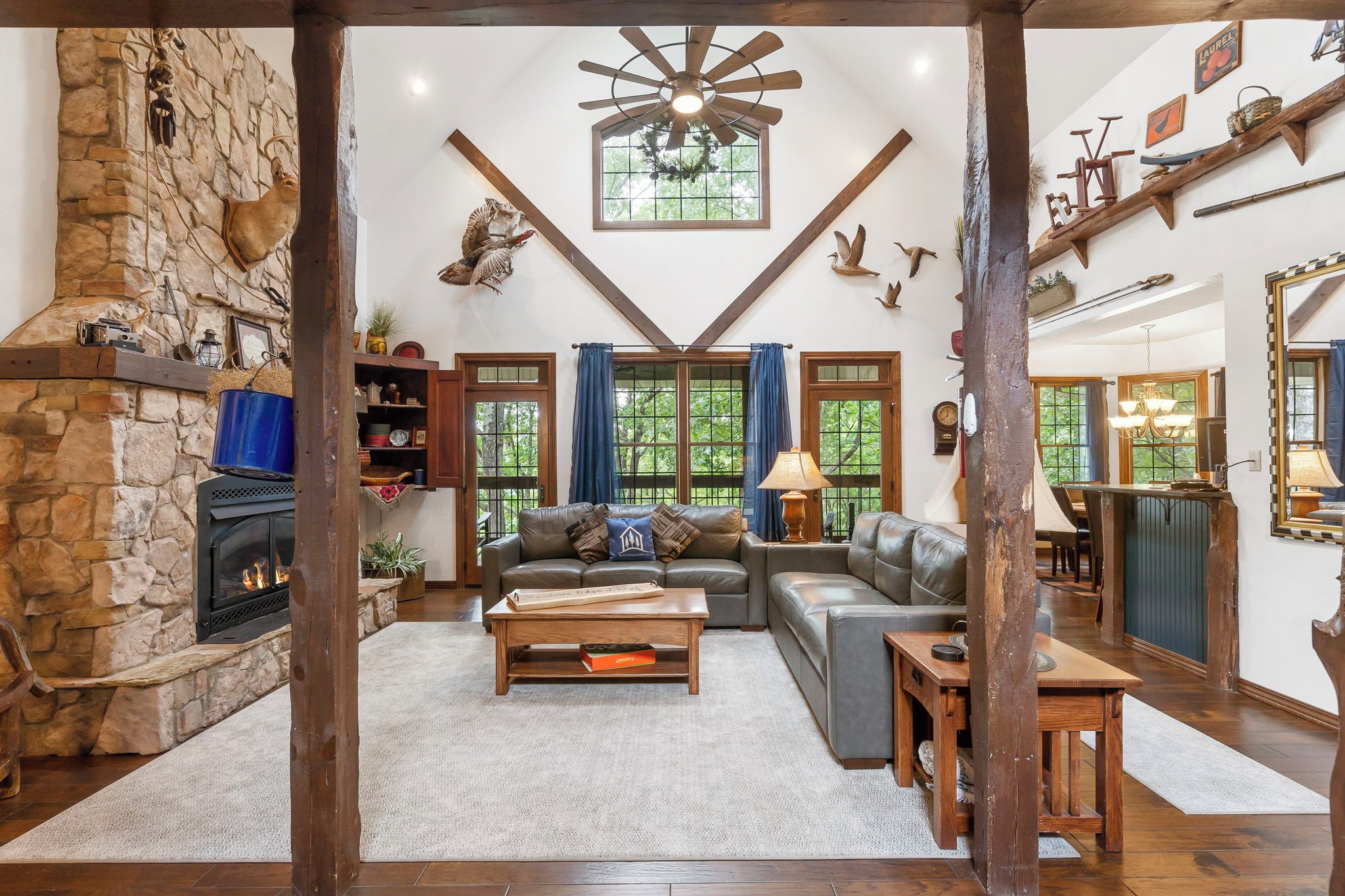 A cozy living room with a stone fireplace, leather sofas, and a wooden ceiling fan.