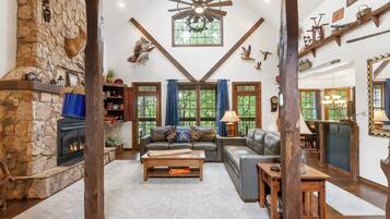 A cozy living room with a stone fireplace, leather sofas, and a wooden ceiling fan.