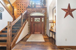 A wooden staircase with a handrail, a stone wall, a wooden door with glass panels, and a star decoration on the wall. - Secluded 40 Acres Near Table Rock, Stunning Views, Games, Community Pool & Car Charger (Blue Eye)