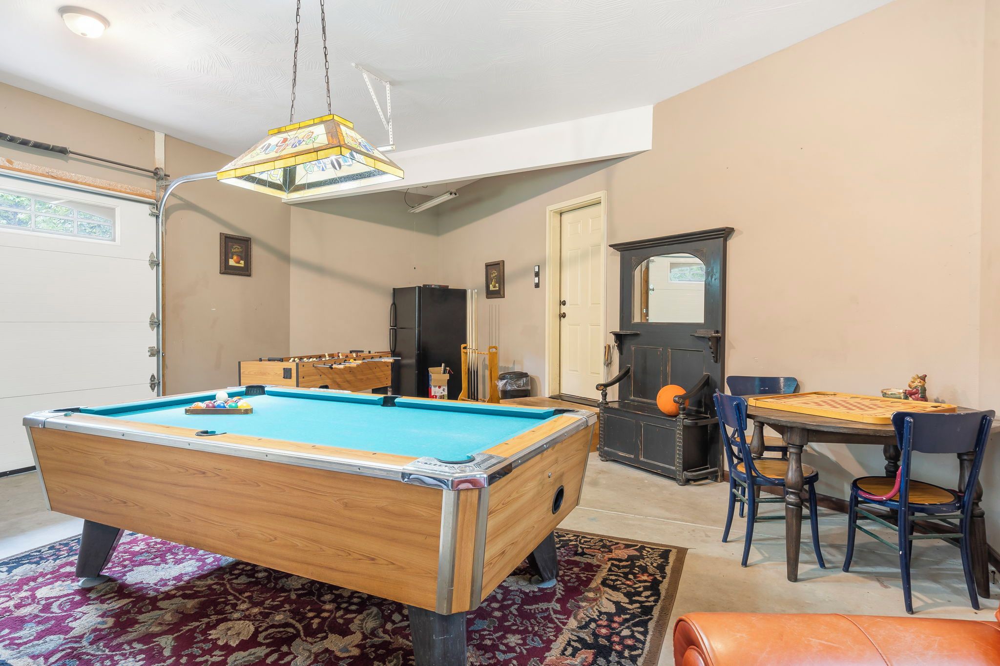 A room with a pool table, a dining table with chairs, a refrigerator, and a door with a mirror.