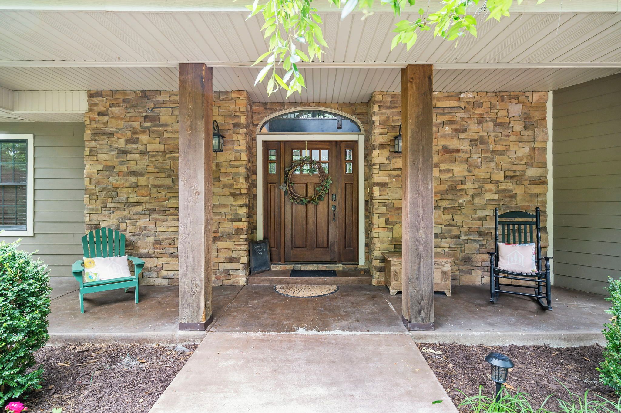 A stone-clad entrance with a wooden door, a bench, and a chair outside.