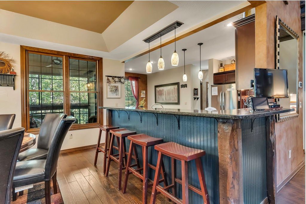 A kitchen with a bar area, wooden stools, and a large window.