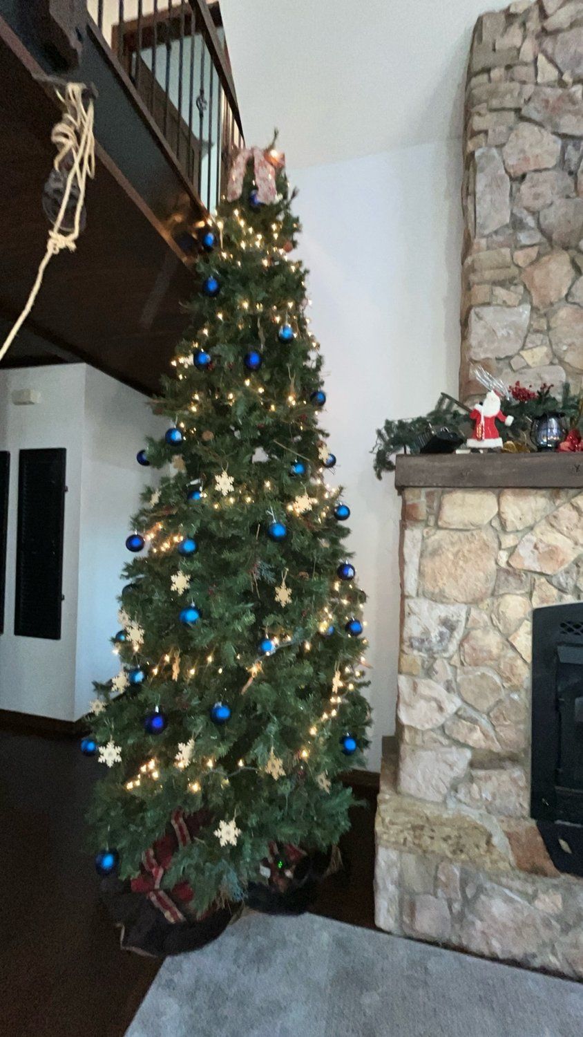 Árvore de Natal com luzes e enfeites em sala de estar com lareira de pedra.