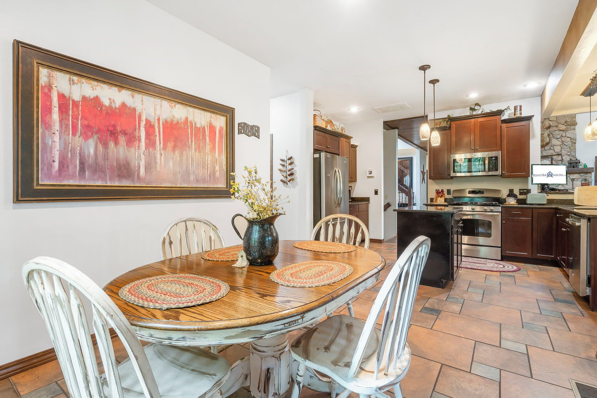 A dining area with a wooden table, white chairs, and a large abstract painting on the wall.