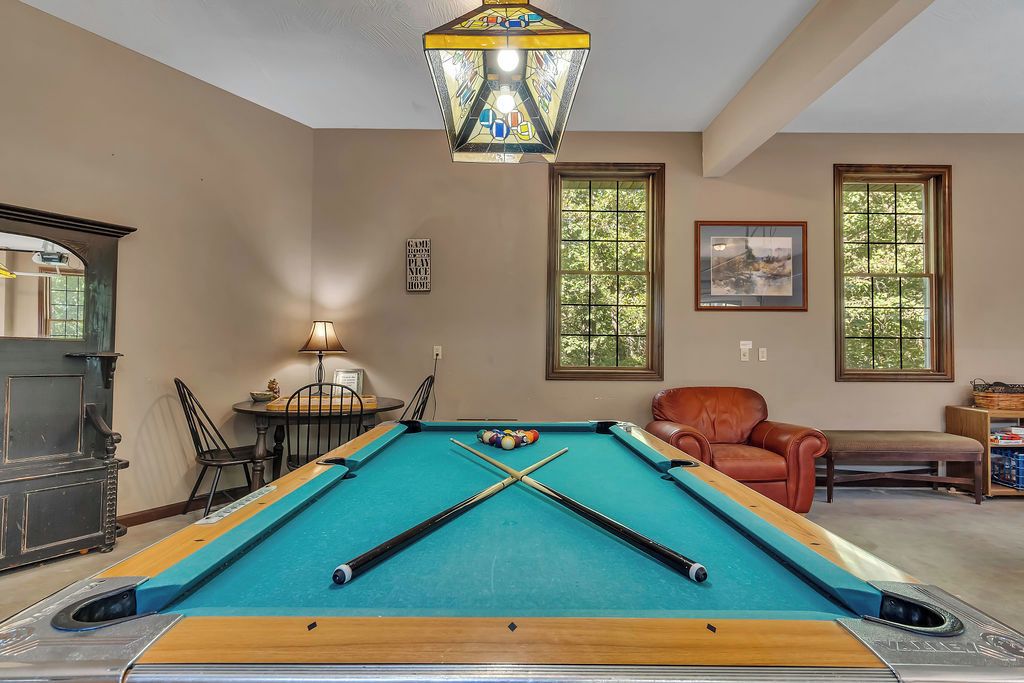 A pool table in a room with large windows, a leather chair, and a lamp.