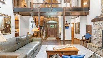 A spacious living area with a leather sofa, a wooden coffee table, and a stone fireplace. A staircase leads to an upper level with a balcony.