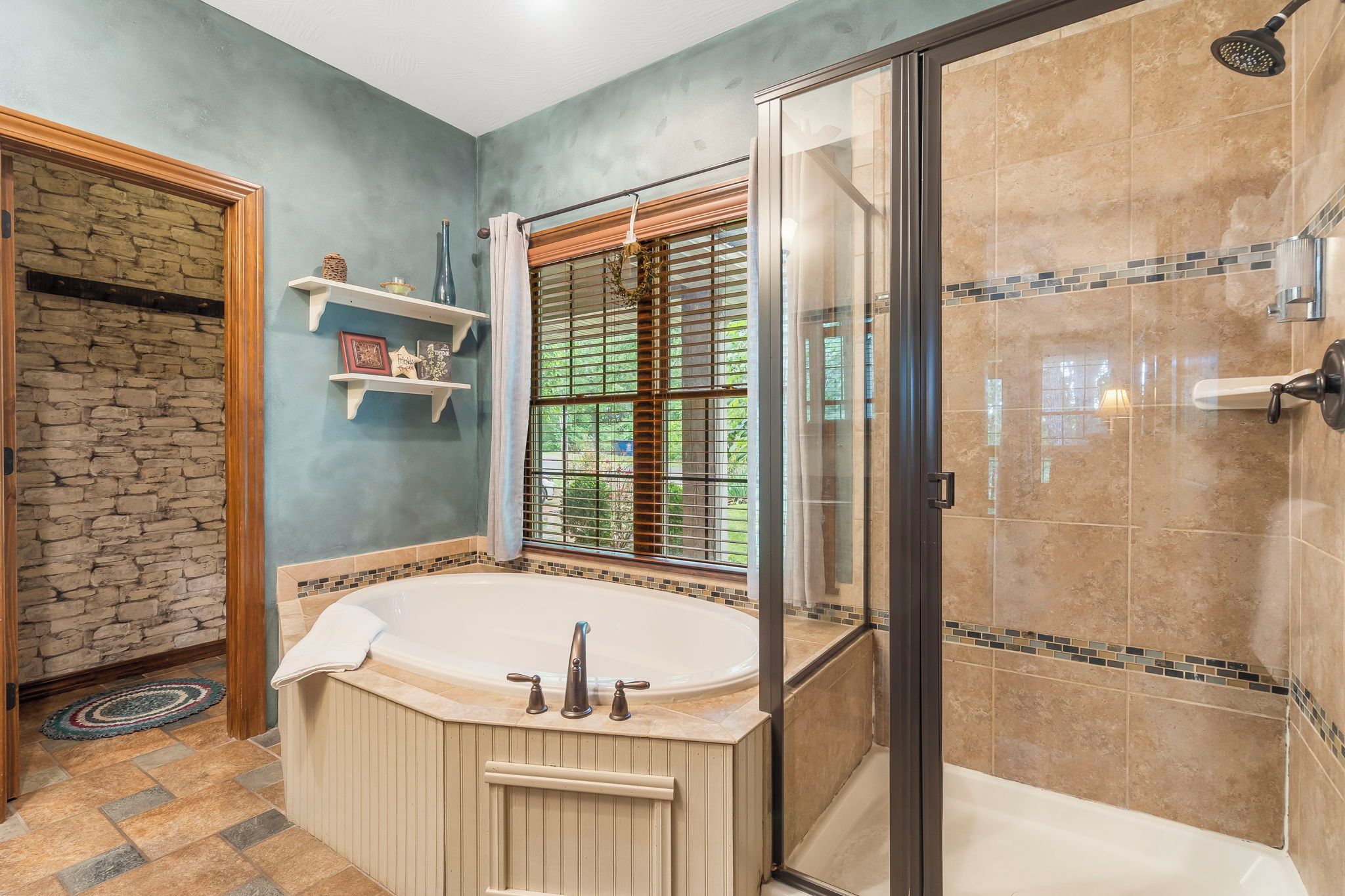 A bathroom with a freestanding bathtub, a glass shower enclosure, and a stone wall.